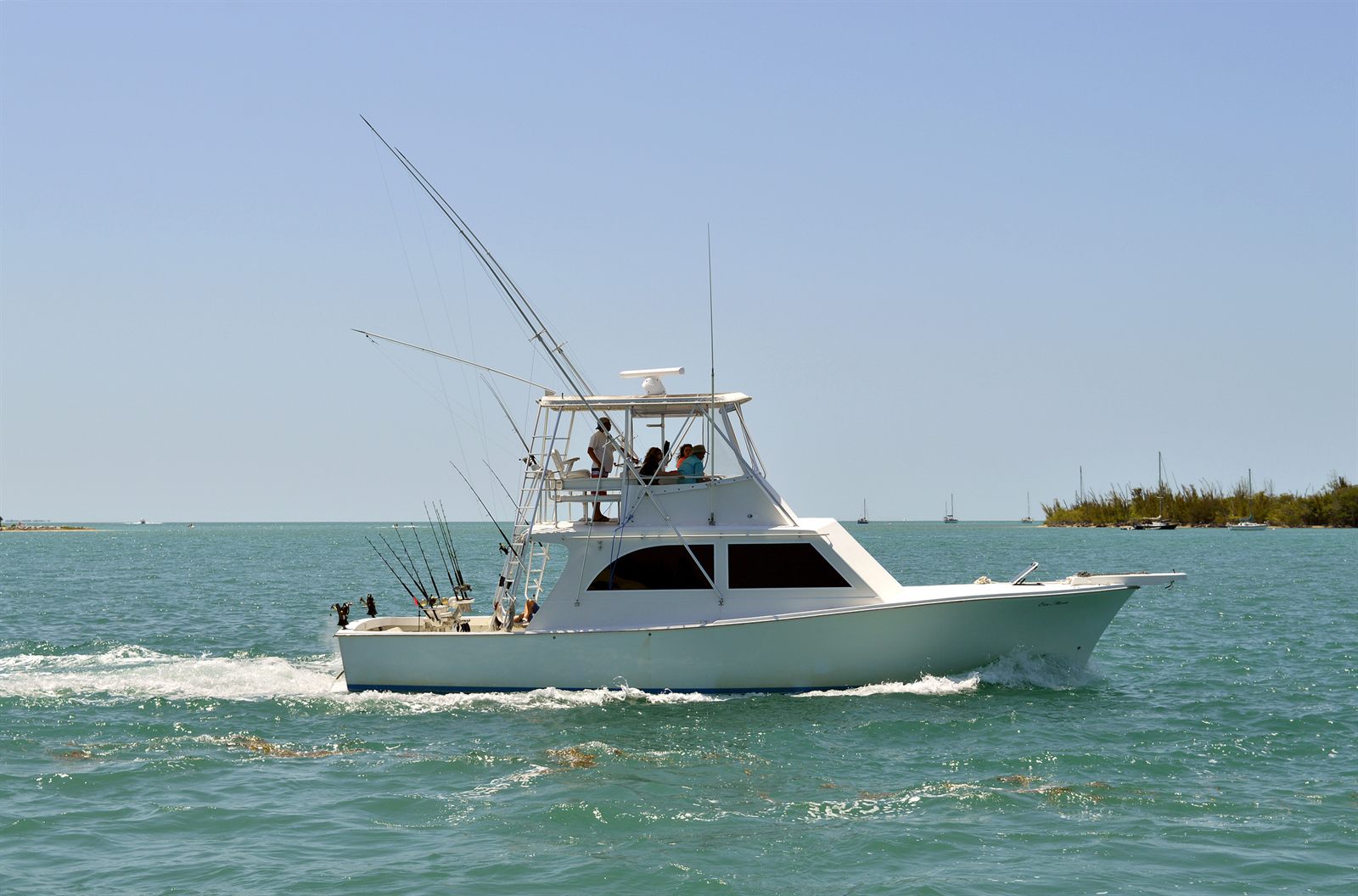 A sport-fishing boat with tall outriggers and a tuna tower running across green coastal water