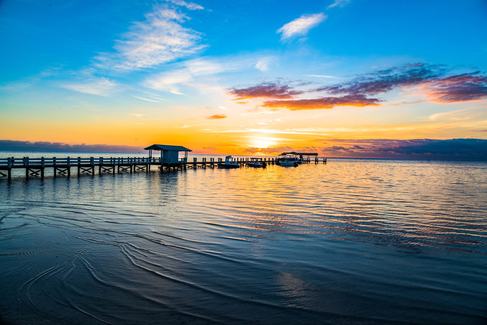 A long dock with a covered end reaching into calm water at sunrise